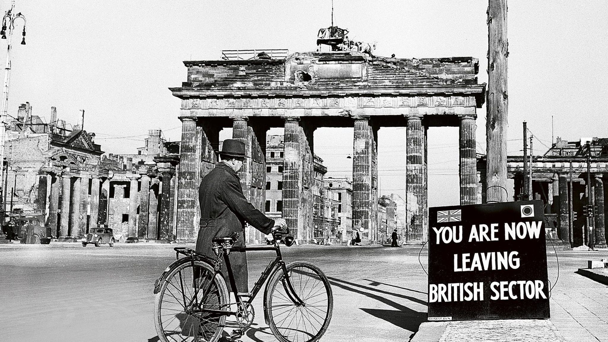 Mann mit Fahrrad auf der Straße vor dem Berliner Tor; davor ein Schild: You Are Now Leaving The British Sector