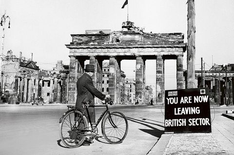 Mann mit Fahrrad auf der Straße vor dem Berliner Tor; davor ein Schild: You Are Now Leaving The British Sector