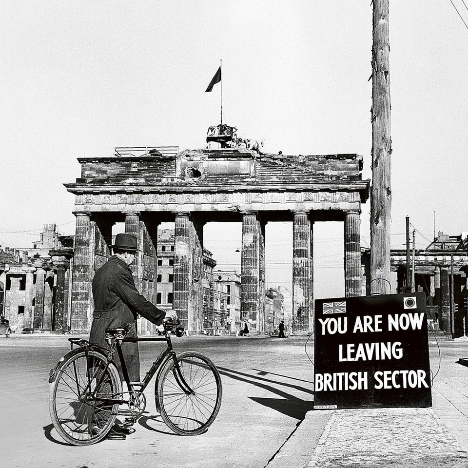 Mann mit Fahrrad auf der Straße vor dem Berliner Tor; davor ein Schild: You Are Now Leaving The British Sector