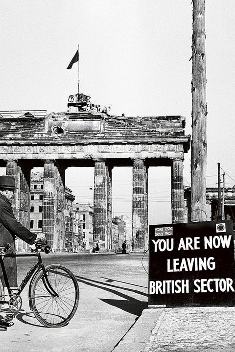 Mann mit Fahrrad auf der Straße vor dem Berliner Tor; davor ein Schild: You Are Now Leaving The British Sector