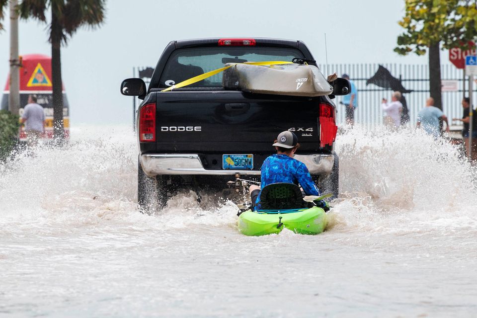 Ein Lastwagen zieht einen Mann auf einem Kajak über eine überflutete Straße