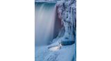 Photographer name: Zhenhuan Zhou     From: Toronto, Canada     Age: 55     Photo title: Frozen     Photo location: Ontario, Canada     Date photo taken: 5 January 2018     Caption: Zhenhuan captured this photo showing parts of Niagara Falls covered in ice.      During spells of cold weather, the mist and spray from Niagara Falls can freeze into ice over the top of the rushing water of the waterfall, giving the appearance that the Falls have frozen whilst the water continues to flow underneath the sheets of ice.      However, there are records that the Falls' waters did stop once in March 1848. Strong winds pushed ice from Lake Erie into the mouth of the Niagara River, blocking the channel completely and stopping the water for about 30 hours. The wind then shifted, and the built-up weight of the water broke through the ice, forcing the Niagara River to flow again.      The photograph offers intricate detail of the icicles that have formed around the building and on the rock face. Icicles are hanging tapering pieces of ice that form when the temperature is below freezing. As water drips off the roof or rock, it freezes and becomes suspended in the shape of a droplet. As more water droplets flow over the surface, they freeze on the way down, and so the process continues until an icicle is formed.      Story behind the photo: Niagara Falls is frozen over.      Media Interviews?     Social media: https://www.facebook.com/ZhouZhenhuan      Camera: Canon EOS 5D Mark IV