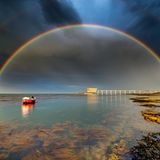 Photographer name: Jamie Russell      From: Shanklin, Isle of Wight, UK      Age: 44      Photo title: Departing Storm Over Bembridge Lifeboat Station     Photo location: Bembridge, Isle of Wight, UK     Date photo taken: May 27 2022      Caption: After chasing storms and showers west to east across the Isle of Wight to capture some incredible rainbows, Jamie reached Bembridge as the final shower left. "In a panic (he) waded into the waist-deep water, fully dressed, just to compose this scene".      Rainbows are optical phenomena that occur when sunlight shines through raindrops. The light is refracted as it enters the raindrop, then reflected off the back of the droplet and then refracted again as it exits and travels towards our eyes. This causes the sunlight to split into different colours. The sun needs to be behind the viewer and needs to be low in the sky. The lower the sun in the sky, the more of an arc of a rainbow the viewer will see. Also, the rain, fog, or other source of water droplets, must be in front of the viewer. The angle at which the light is scattered is different for everyone, which means that every rainbow is unique to the observer.      Double rainbows form when sunlight is reflected twice within a raindrop. They are relatively common, especially when the sun is low in the sky, such as in the early morning and late afternoon. The second rainbow is fainter, and more 'pastel' in tone and a key feature of a double rainbow is that the colour sequence in the second rainbow is reversed.      Story behind the photo: I had been chasing showers and storms from west to east across the island in an attempt to capture some of the incredible rainbows. I reached Bembridge as the final shower departed and in a panic waded in to waist deep water, fully dressed just to compose this scene!      Media interviews:      Social media:          https://www.facebook.com/Island.visions.photography/  https://www.instagram.com/island_visions_photography/      Camera: Nikon d7500, Sigma 10-20 lens. Exposure time 1/200, f10, ISO 400