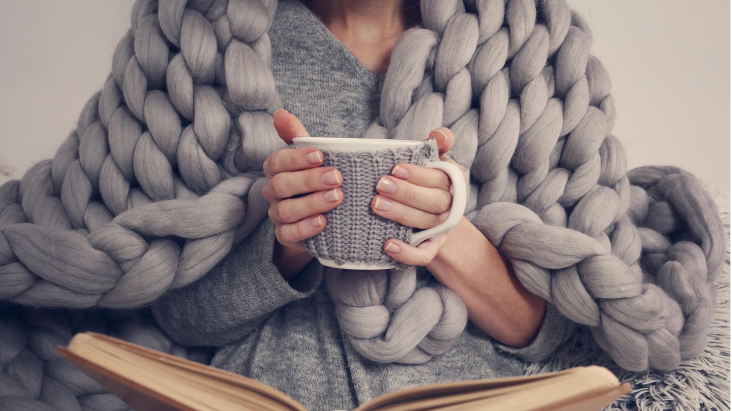 Eine Frau mit Tee in der Hand und einer Kuscheldecke