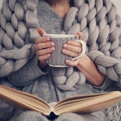 Eine Frau mit Tee in der Hand und einer Kuscheldecke