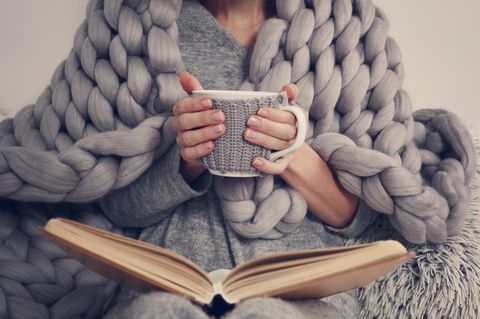 Eine Frau mit Tee in der Hand und einer Kuscheldecke