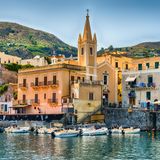 Blick auf den Hafen von Lipari mit Booten und einem Kirchturm. Im Hintergrund sind Berge