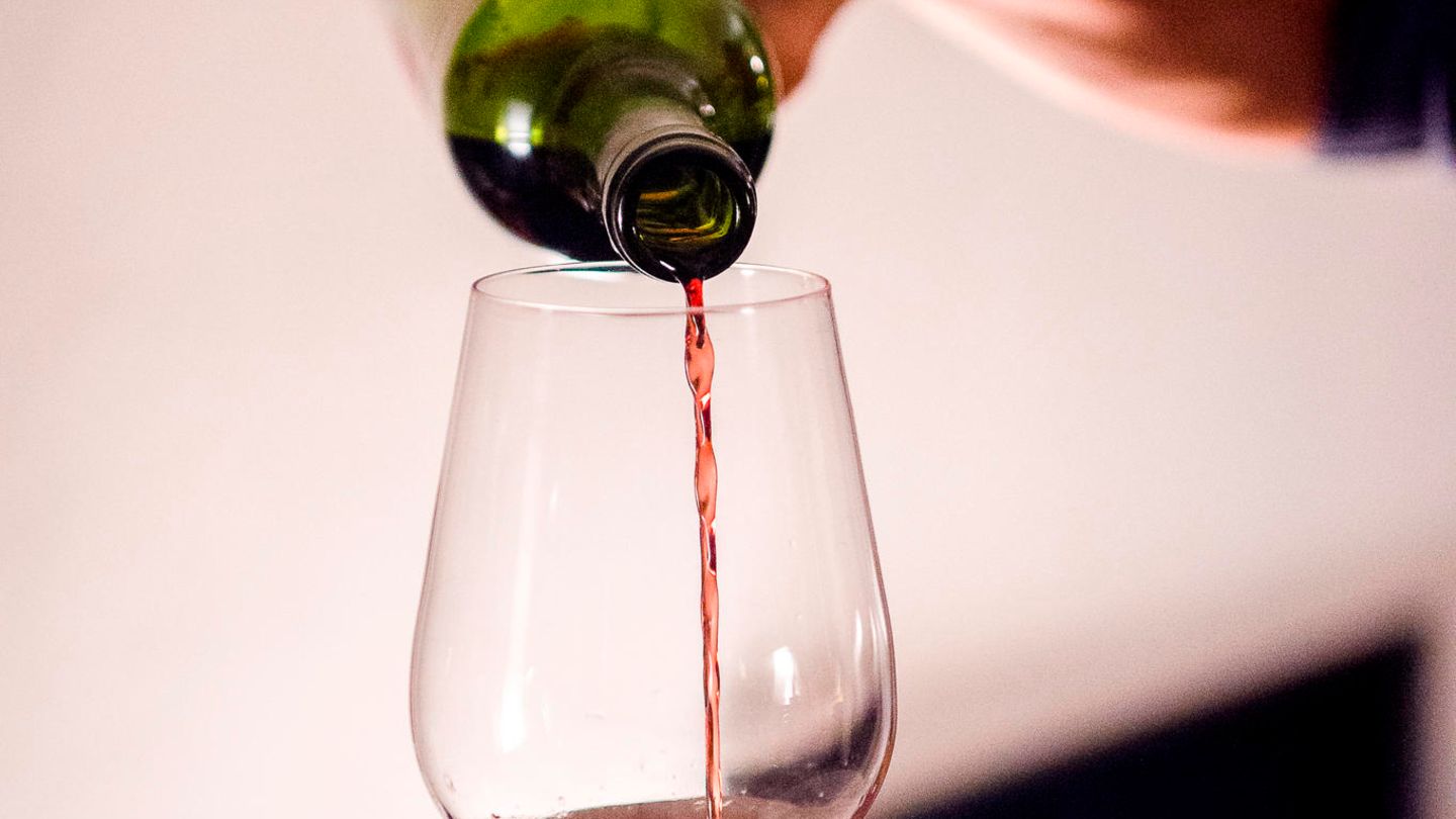 Eine Frau gießt zuhause Wein in ein Glas Eine Frau gießt zuhause Wein in ein Glas