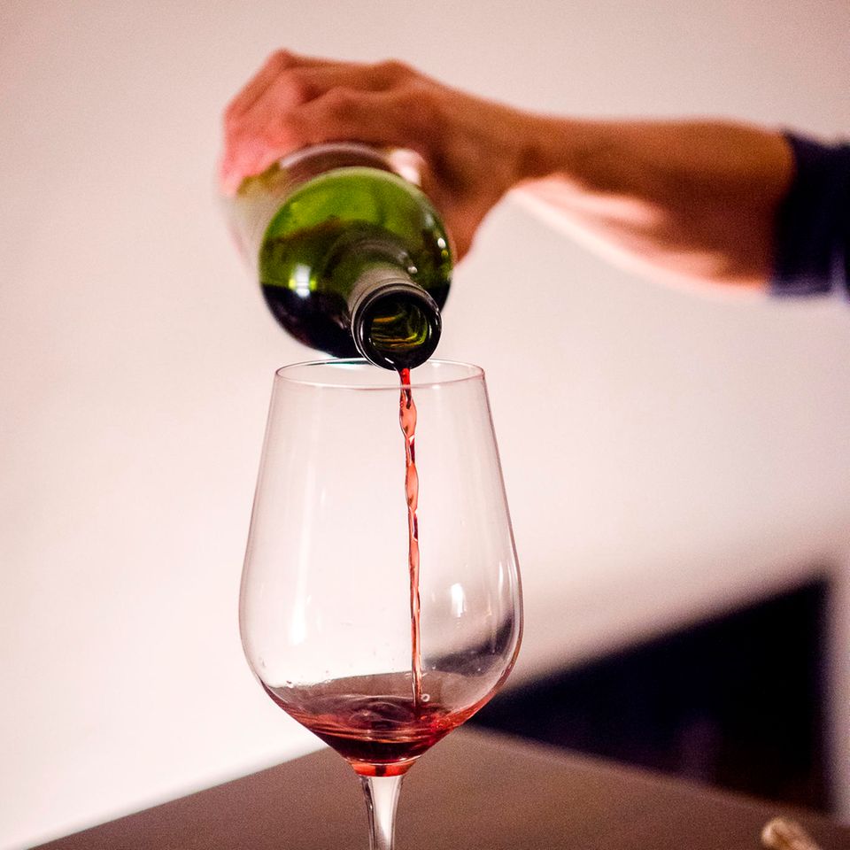 Eine Frau gießt zuhause Wein in ein Glas