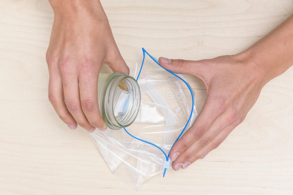 Winter-Basteln: Eine klare Flüssigkeit wird aus einem Glas in eine wiederverschließbare Plastiktüte gekippt.