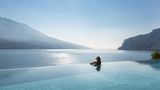 Eine Frau in einem Infinitypool, hinter dem der Gardasee liegt