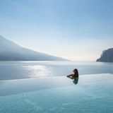 Eine Frau in einem Infinitypool, hinter dem der Gardasee liegt
