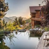 Naturpool mit Blick auf die Berge, auf der rechten Seite steht ein großes Haus aus Holz