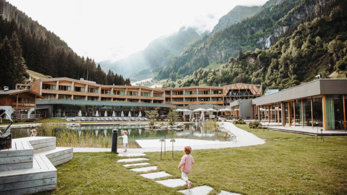 Kategorie Familie: Feuerstein in Südtirol, Italien Kleine Kinder laufen vor dem Hotel entlang, das zwischen den Bergen liegt
