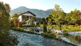 Ein kleiner Fluss fließt im Vordergrund an dem Hotel vorbei. Im Hintergrund sind Berge zu sehen