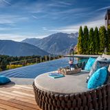Eine große Liege vor einem Infinity-Pool, im Hintergrund sind Berge