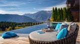 Eine große Liege vor einem Infinity-Pool, im Hintergrund sind Berge