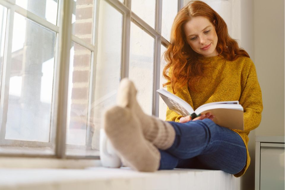 Eine Frau sitzt auf der Fensterbank und liest