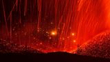Glühende Lava zieht rote Bahnen und ergießt sich auf den Hängen einer kahlen Berglandschaft. Vereinzelt ragen nackte Baumstämme aus dem Erdreich. "Feuerwelten" nannte Eduardo Blanco Mendizabal diese Nachtaufnahme einer Eruption. 2021 kam es zu einer längeren Phase vulkanischer Aktivität  auf der Cumbre Vieja, einer 14 Kilometer langen Vulkankette auf La Palma.