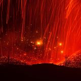 Glühende Lava zieht rote Bahnen und ergießt sich auf den Hängen einer kahlen Berglandschaft. Vereinzelt ragen nackte Baumstämme aus dem Erdreich. "Feuerwelten" nannte Eduardo Blanco Mendizabal diese Nachtaufnahme einer Eruption. 2021 kam es zu einer längeren Phase vulkanischer Aktivität  auf der Cumbre Vieja, einer 14 Kilometer langen Vulkankette auf La Palma.