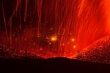 Glühende Lava zieht rote Bahnen und ergießt sich auf den Hängen einer kahlen Berglandschaft. Vereinzelt ragen nackte Baumstämme aus dem Erdreich. "Feuerwelten" nannte Eduardo Blanco Mendizabal diese Nachtaufnahme einer Eruption. 2021 kam es zu einer längeren Phase vulkanischer Aktivität  auf der Cumbre Vieja, einer 14 Kilometer langen Vulkankette auf La Palma.