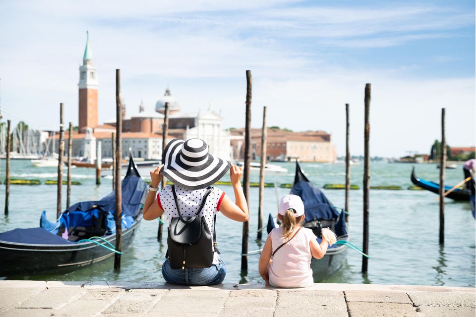 Frau und Kleinkind sitzen vor Booten in Venedig