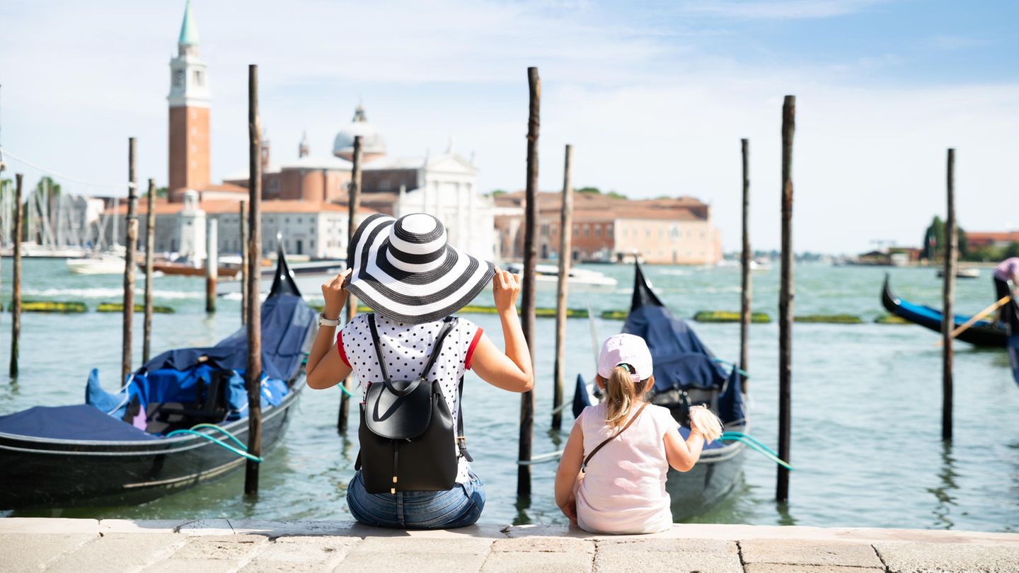 Frau und Kleinkind sitzen vor Booten in Venedig