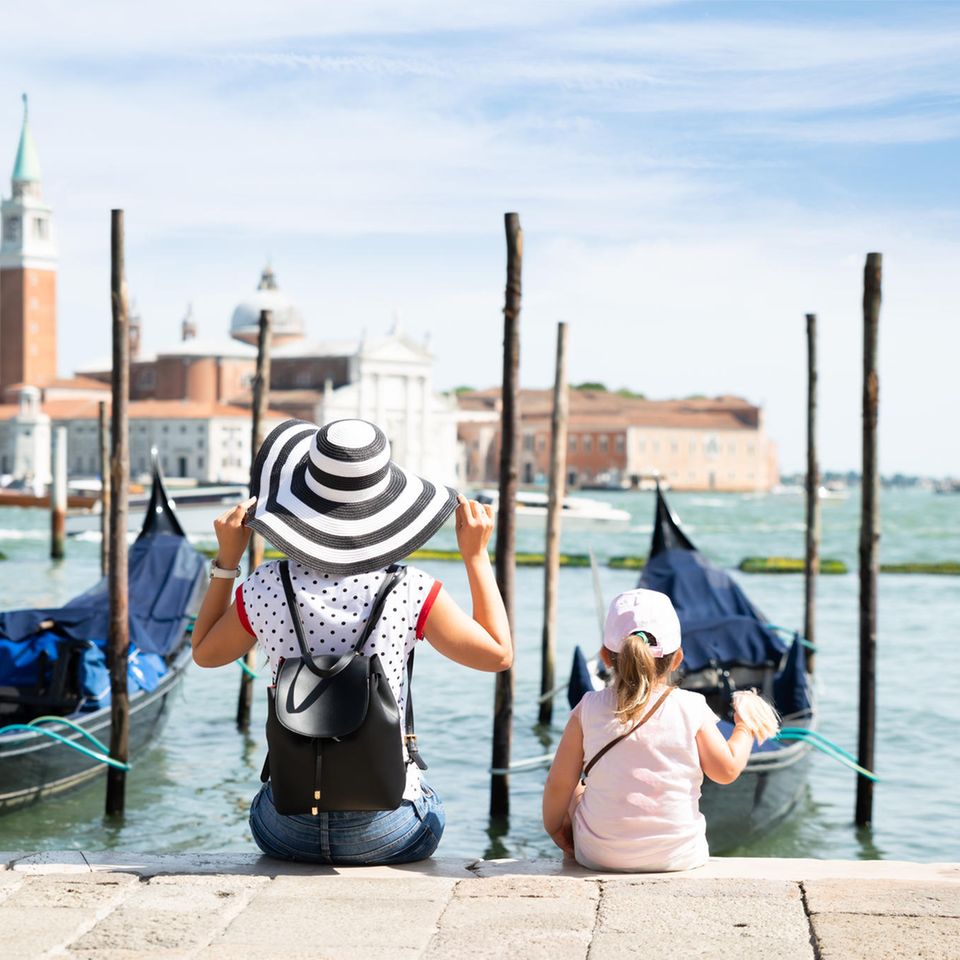 Frau und Kleinkind sitzen vor Booten in Venedig