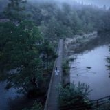 Eine Person läuft in einem weißen Gewand bei Nebel über eine Brücke