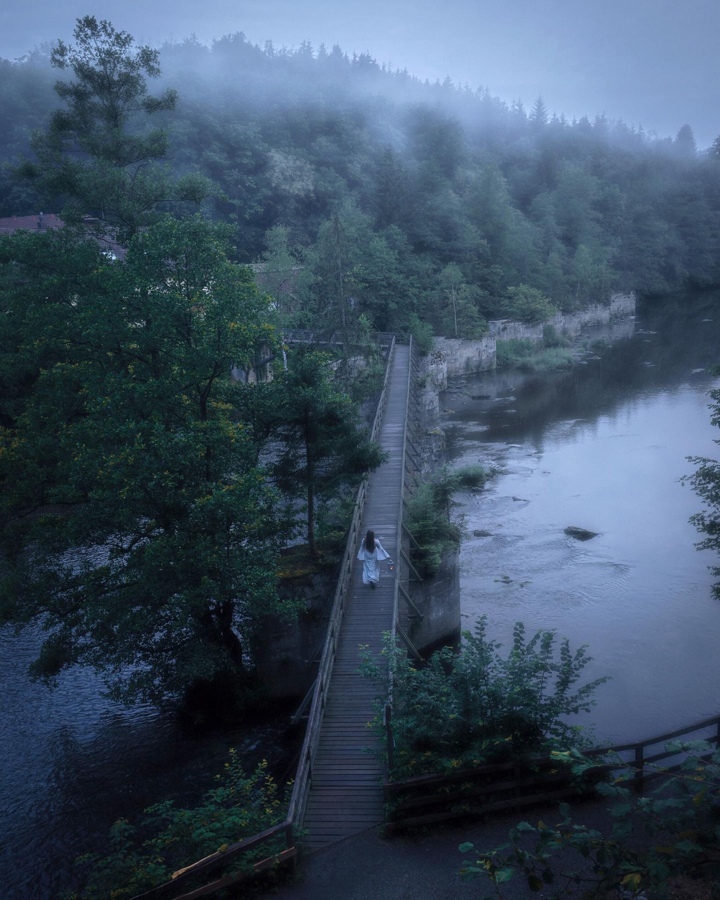Eine Person läuft in einem weißen Gewand bei Nebel über eine Brücke
