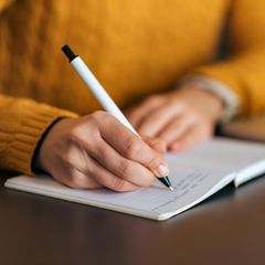 Frau schreibt mit Stift in ein Notizbuch