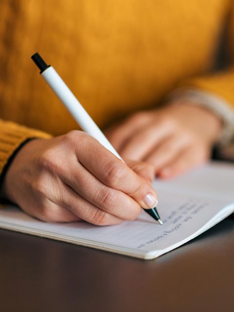 Frau schreibt mit Stift in ein Notizbuch