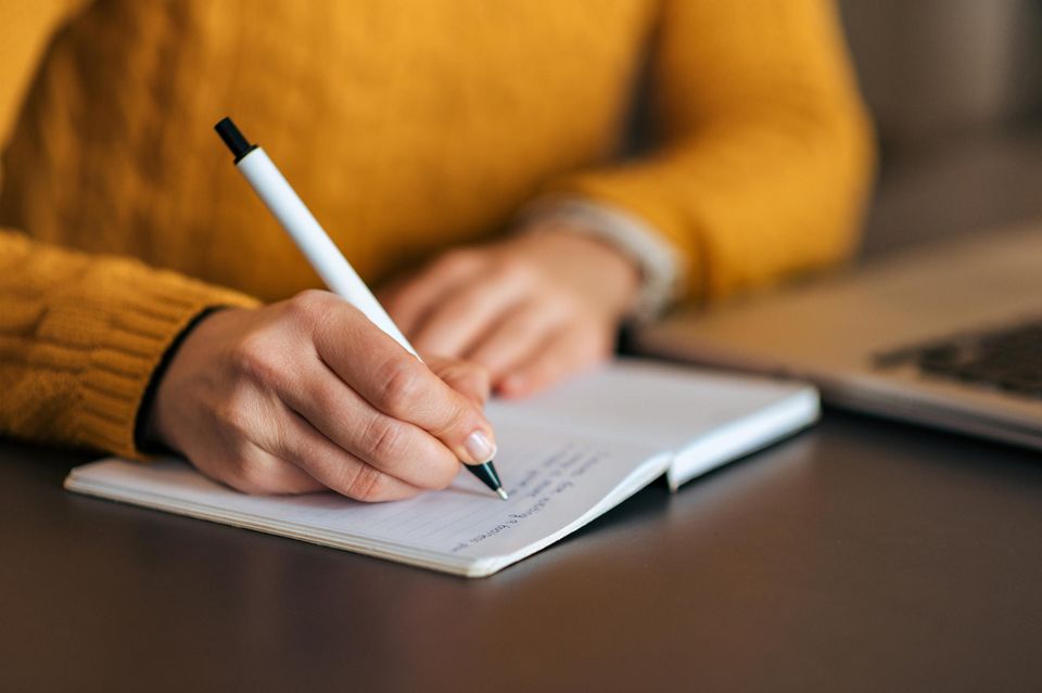 Frau schreibt mit Stift in ein Notizbuch 1.4982