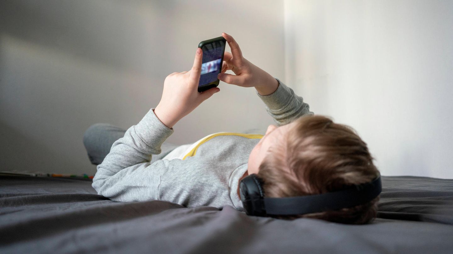 Ein Junge liegt auf dem Bett und schaut einen Film auf seinem Smartphone