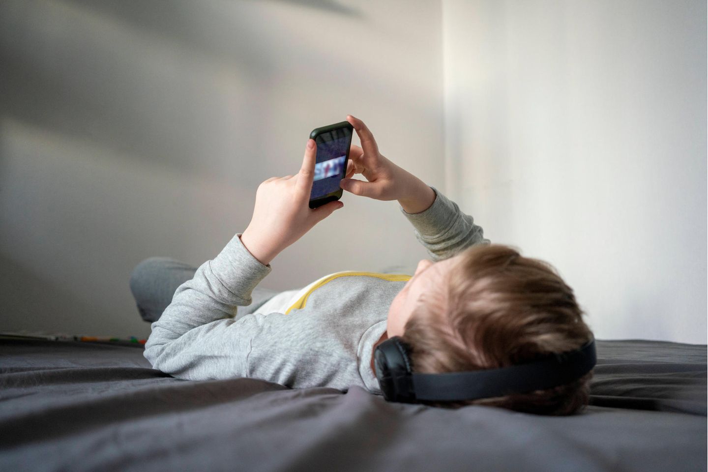 Ein Junge liegt auf dem Bett und schaut einen Film auf seinem Smartphone