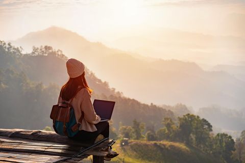 Eine Frau sitzt mit ihrem Laptop in den Bergen