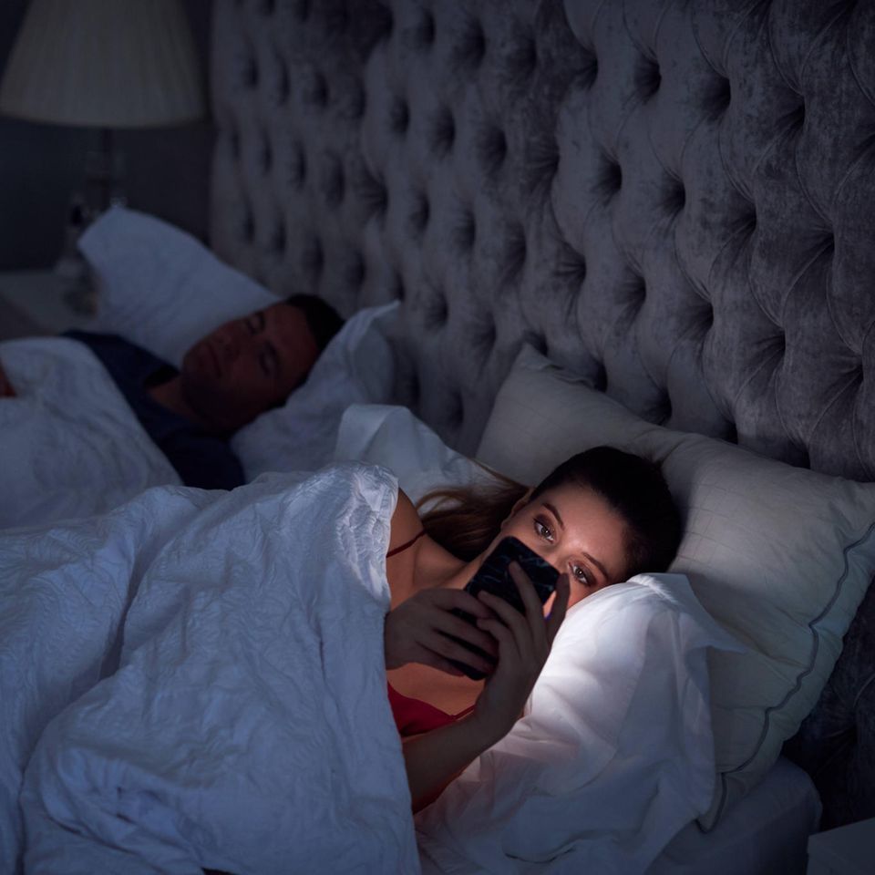 Eine Frau liegt wach im Bett und schaut auf ihr Handy