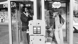 Zwei Männer telefonieren in zwei Telefonzellen