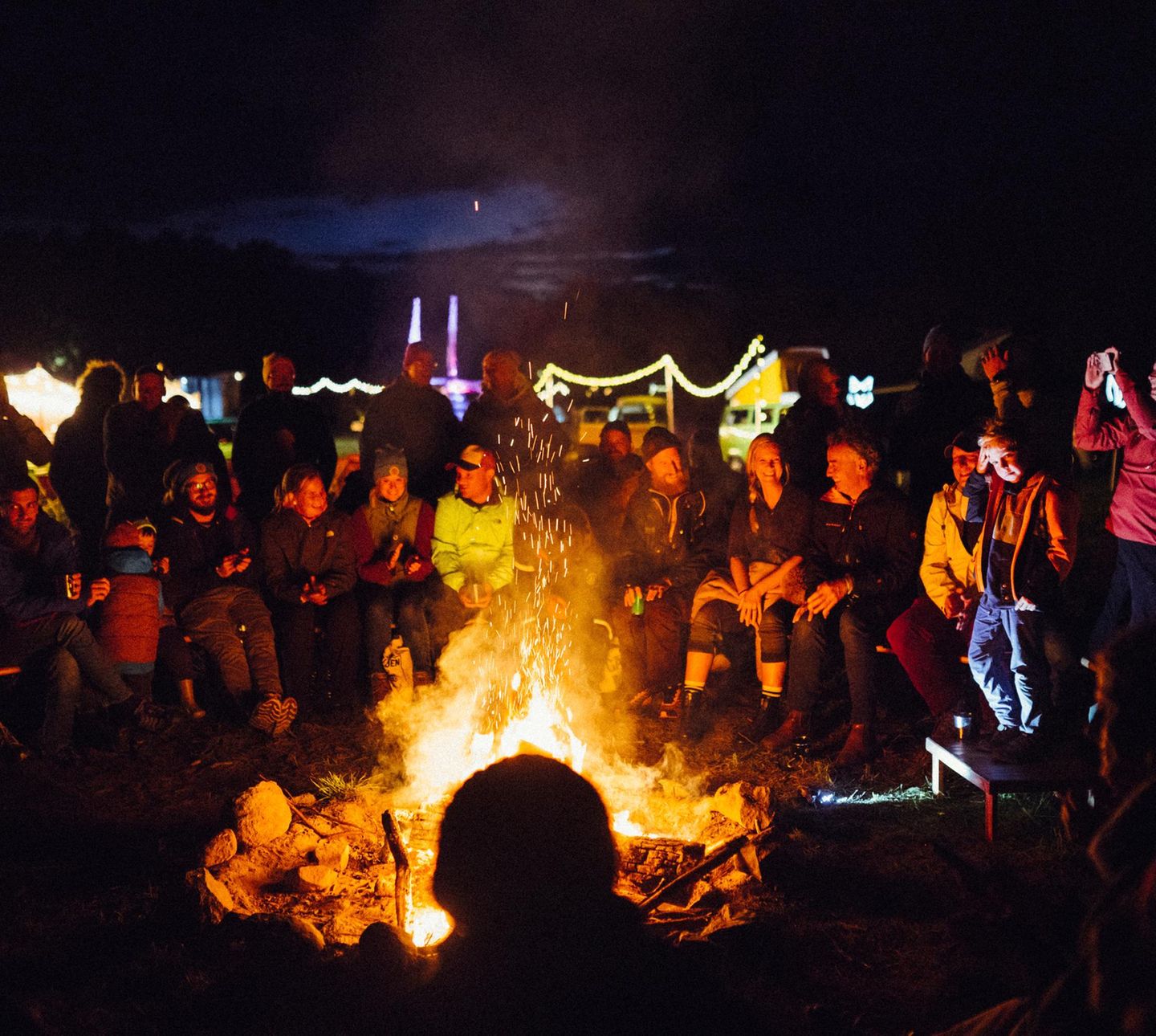 Eine größere Gruppe sitzt am Abend um ein Lagerfeuer herum