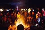 Eine größere Gruppe sitzt am Abend um ein Lagerfeuer herum