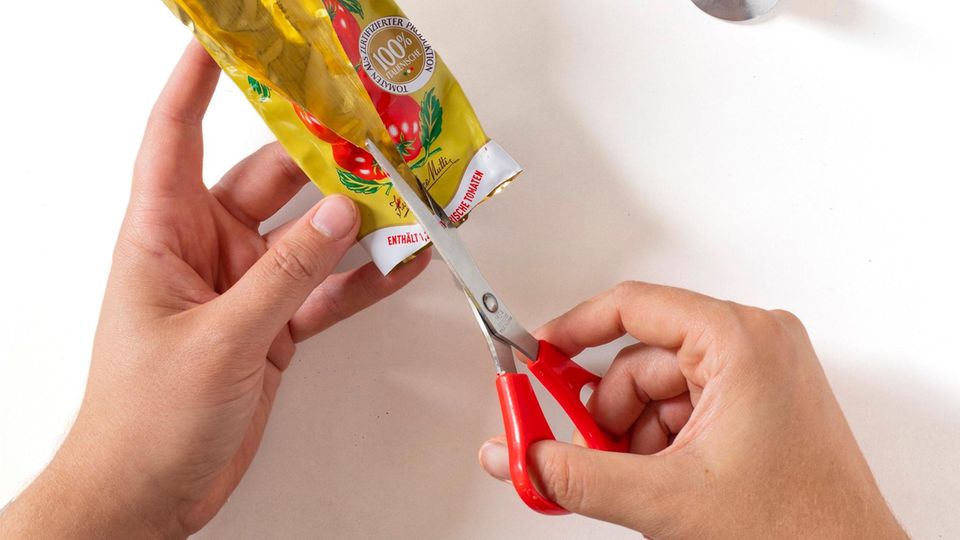 Eine Tomatenmarktube wird aufgeschnitten. Eine Tomatenmarktube wird aufgeschnitten.