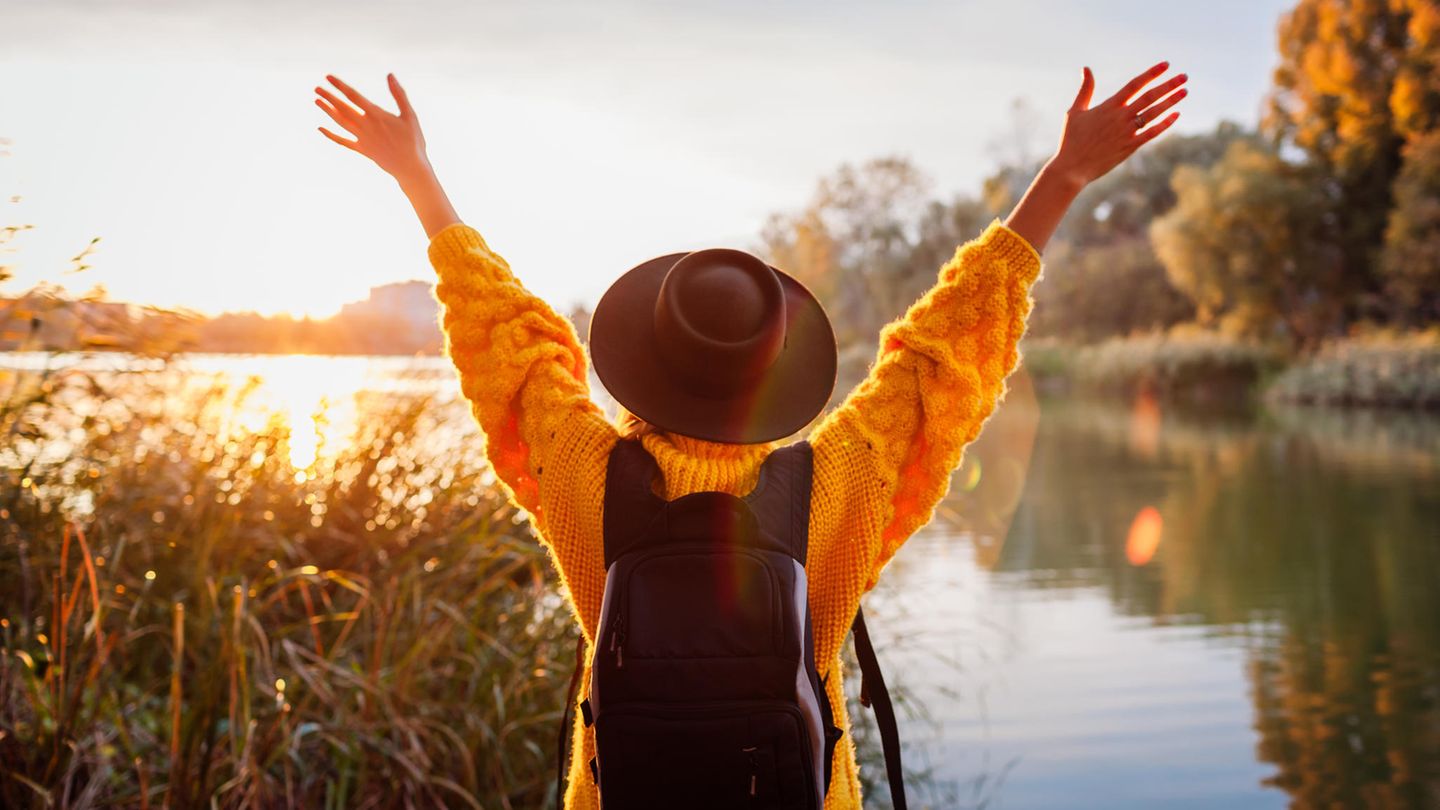 Black Friday und Cyber Monday 2022: Eine Frau in gelbem Pullover steht vor einem See. Black Friday und Cyber Monday 2022: Eine Frau in gelbem Pullover steht vor einem See.