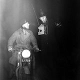 Schwarz-weiß-Foto eines Polizisten, der einem Motorradfahrer durch den Smog hilft