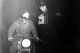 Schwarz-weiß-Foto eines Polizisten, der einem Motorradfahrer durch den Smog hilft