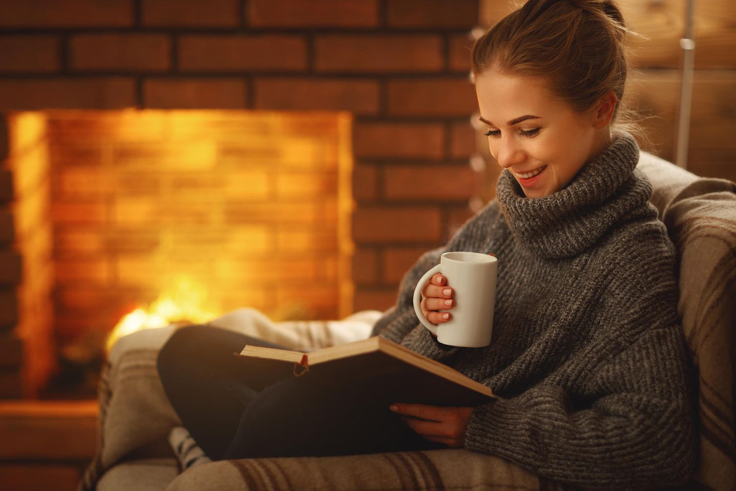 Eine junge Frau sitzt mit einem Buch vor dem Kamin