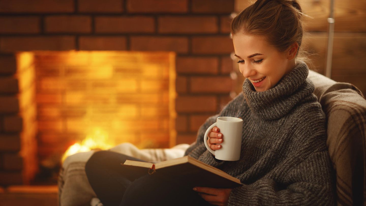 Eine junge Frau sitzt mit einem Buch vor dem Kamin