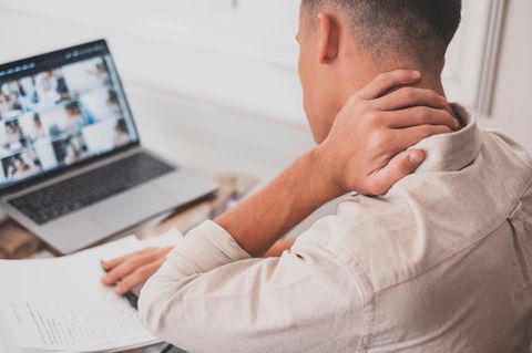 Ein Mann sitzt vor dem Laptop und fährt mit der Hand über den verspannten Nacken