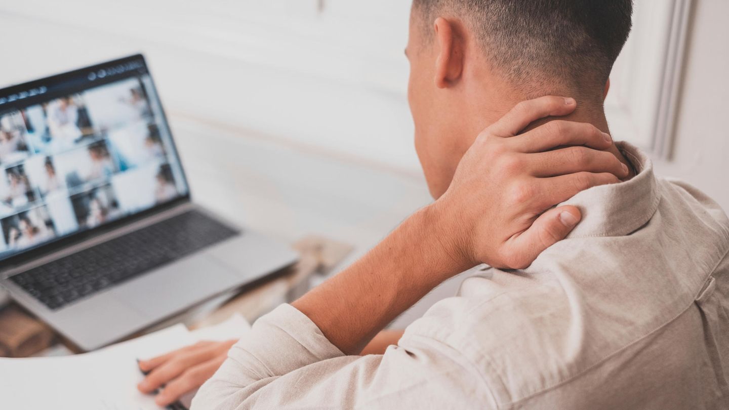 Ein Mann sitzt vor dem Laptop und fährt mit der Hand über den verspannten Nacken