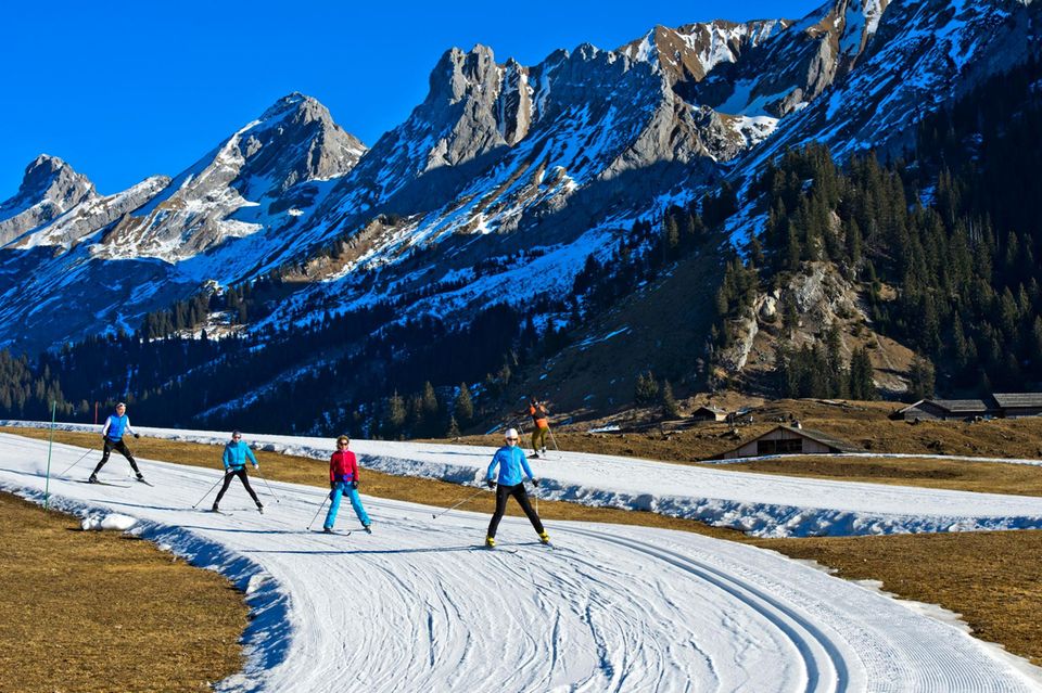 Die Gegenwart des Wintersports: Skilangläufer fahren in einem schneearmen Winter auf Kunstschnee-Loipen vor dem Massif des Aravis