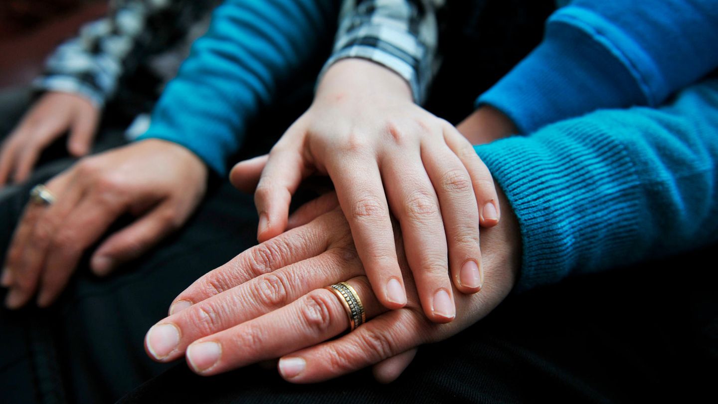 Ein Kind legt die Hand auf die des Vaters, der einen Ehering trägt